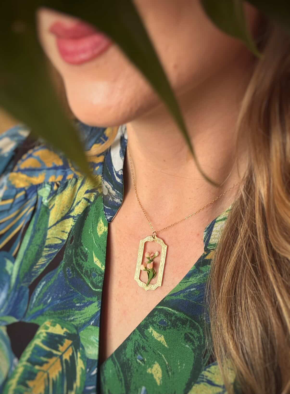 Close-up of a person wearing a gold necklace with a green pendant, set against a blurred background.