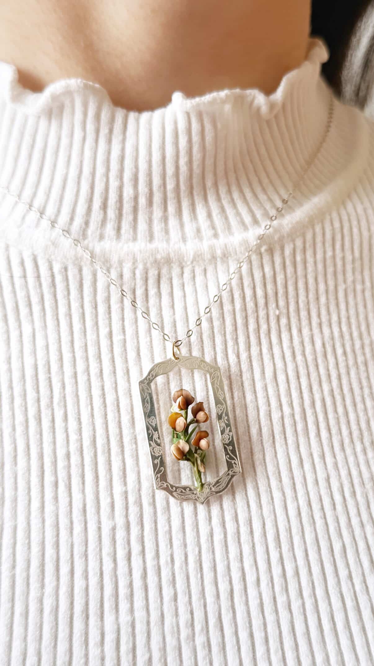 Necklace with a pendant featuring small flowers worn by a person on a white ribbed sweater.